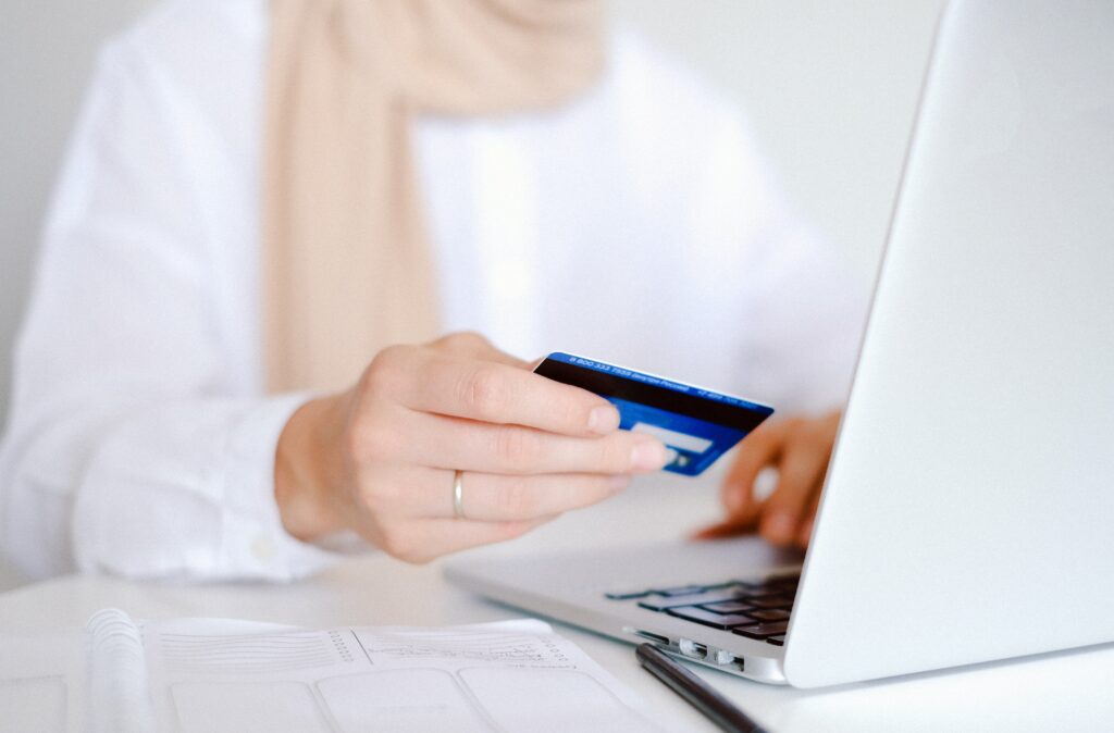 person in white long sleeve shirt holding credit card in front of computer